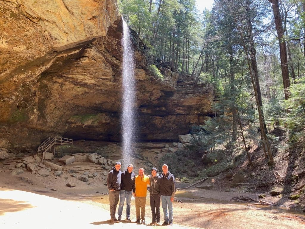 Visitors standing at the base of a tall waterfall in Hocking Hills.