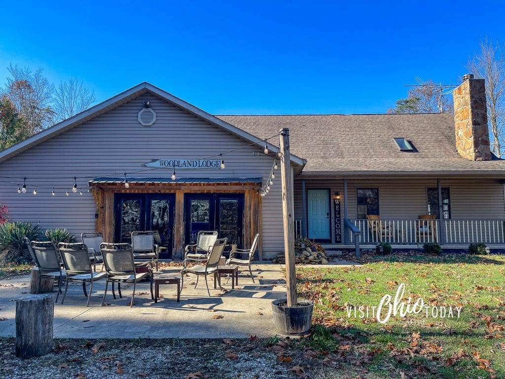Exterior photo of The Woodlands at Hocking Hills lodge with patio chairs and blog title overlay