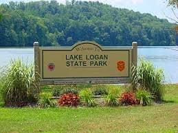 Lake Logan State Park entrance sign beside calm lake and grassy area