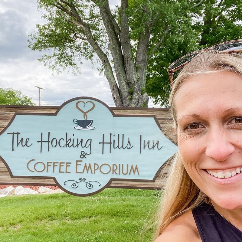 Photo of Debbie Todd of The Woodlands at Hocking Hills in front of the shop sign of The Hocking Hills Coffee Emporium.