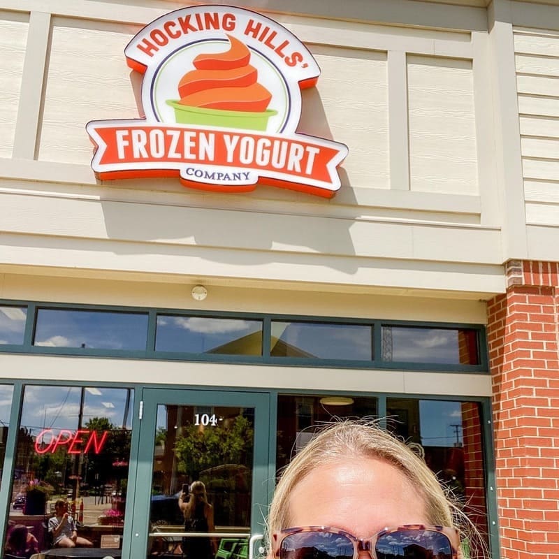A photo of Debbie Todd of The Woodlands at Hocking Hills at the shop sign of Hocking Hills Frozen Yogurt Company.